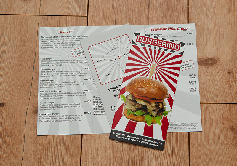 Das Bild zeigt einen Flyer. Aufgeklappt zeigt er auf der Rückseite die Speisenkarte, auf der Vorderseite einen Burger, das Firmenlogo und einen Lageplan.
